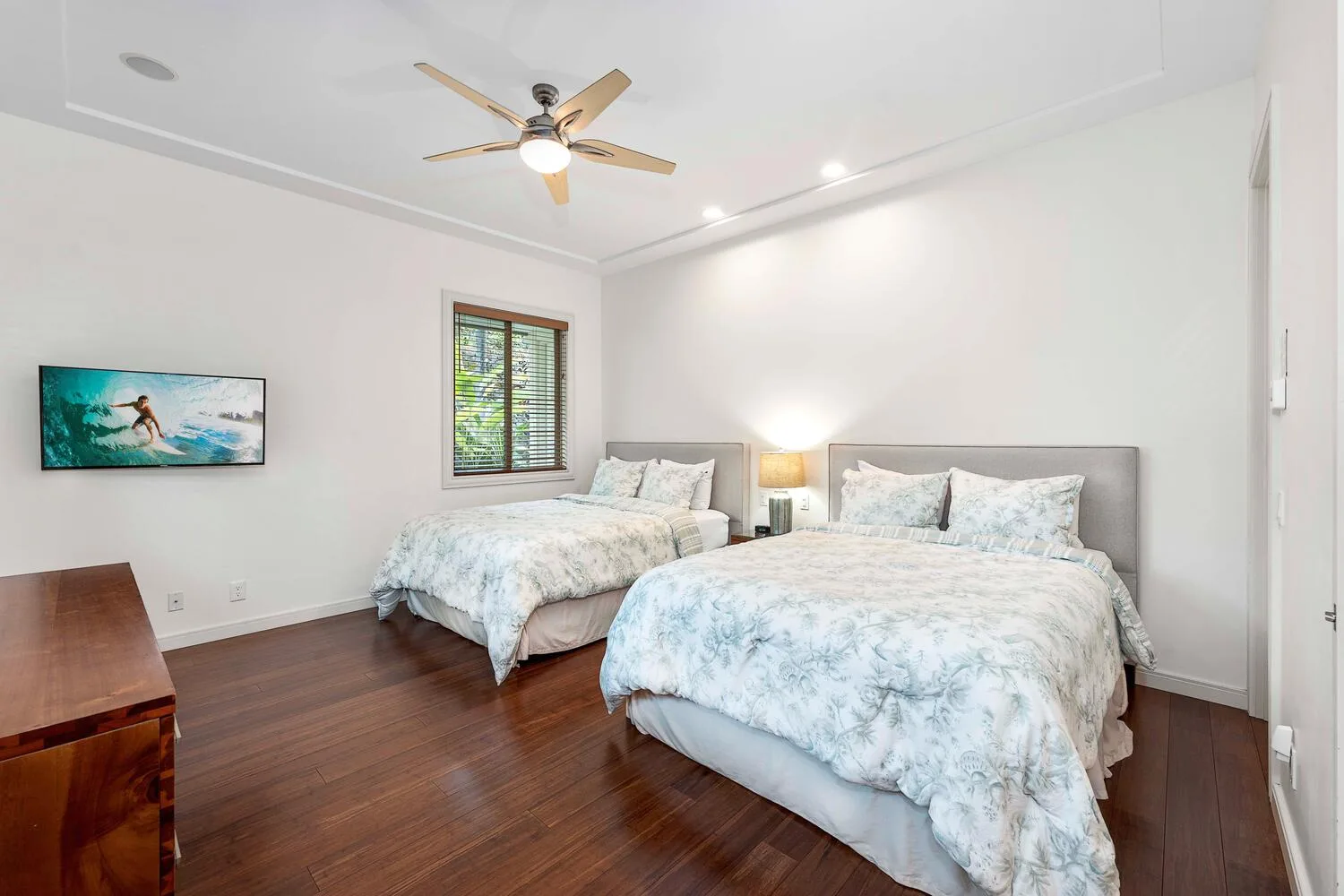 A bedroom with two beds, pale bedding, and a ceiling fan.