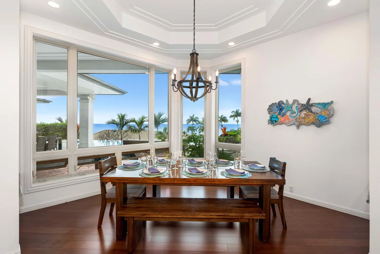 A dining room with a set table beside large windows overlooking the water.