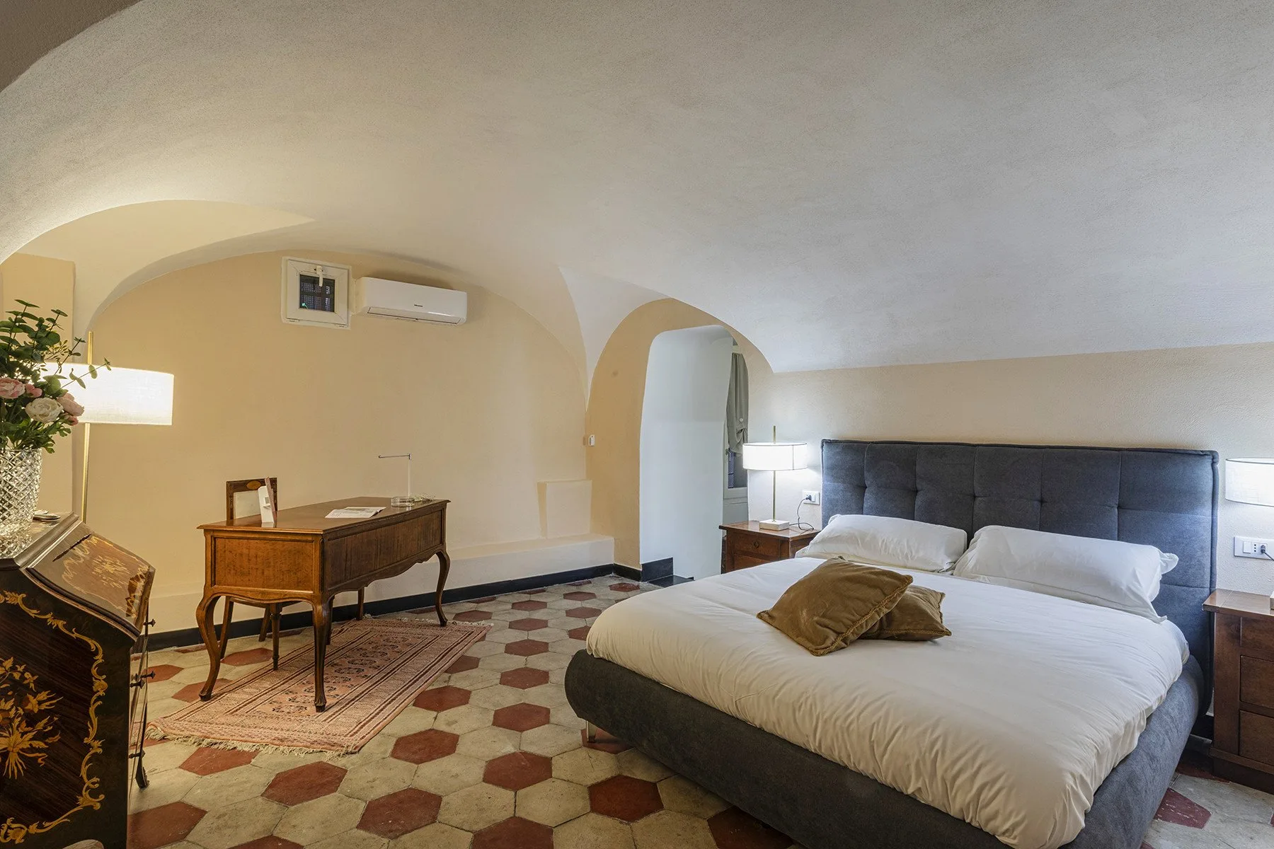 A bedroom with a large bed, bedside tables, and patterned tile flooring.
