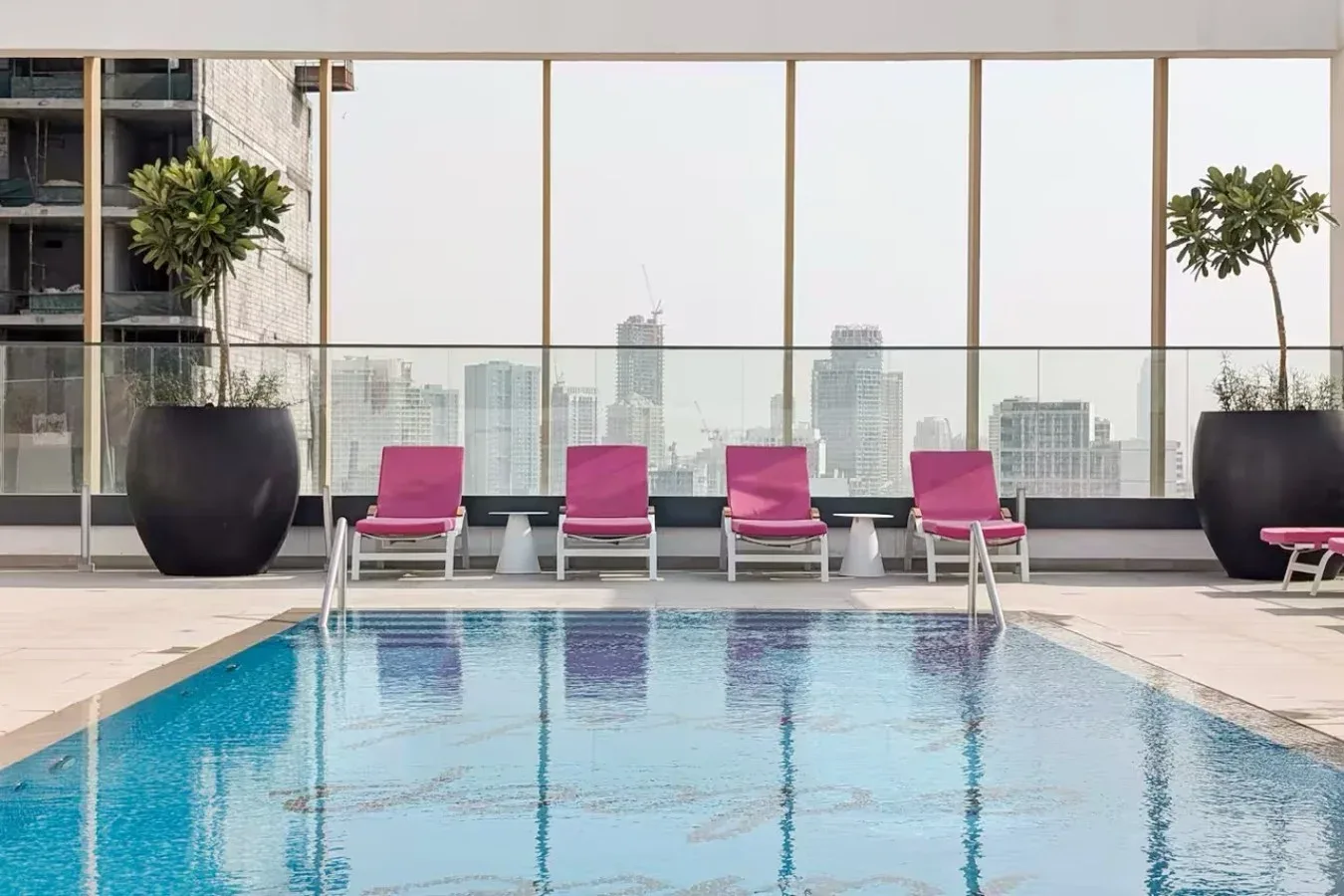 Una piscina en la azotea mira hacia la ciudad, con tumbonas rosas junto al borde.