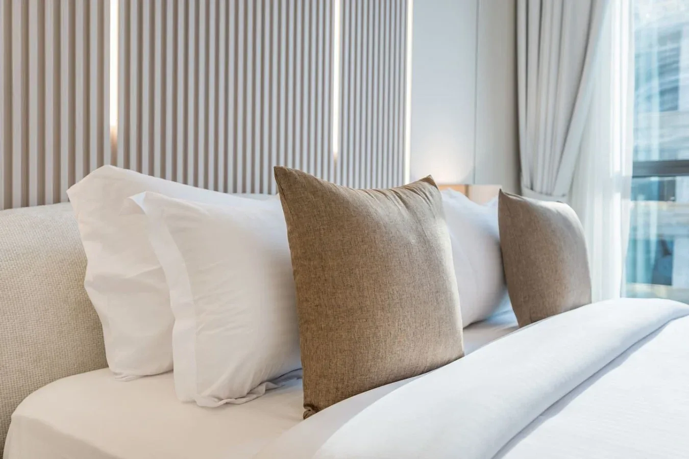 Una cama bien tendida con ropa de cama blanca y cojines decorativos.