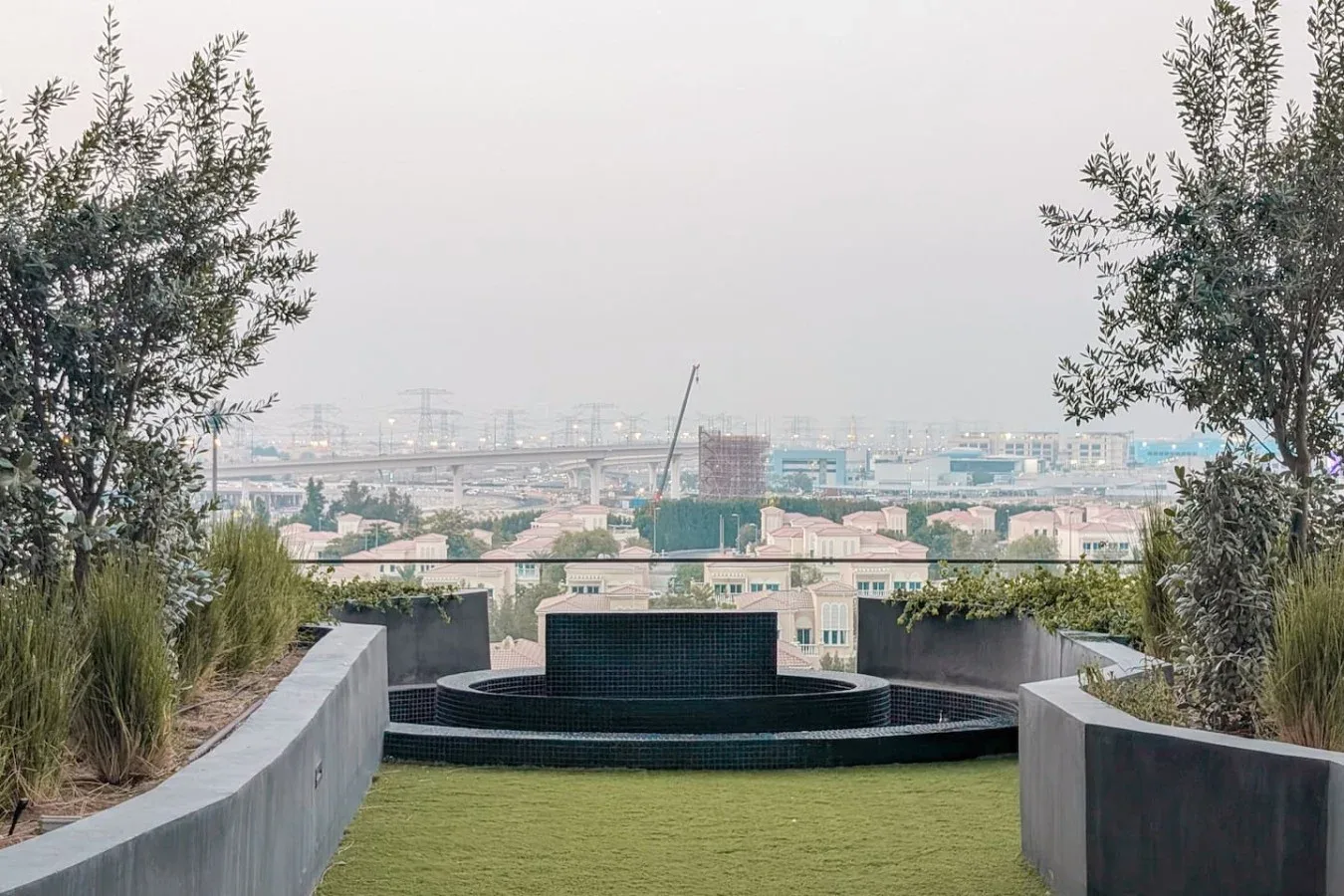 Una terraza ajardinada ofrece vistas al horizonte urbano, con una fuente circular al frente.