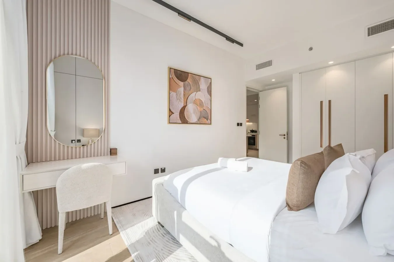 Un dormitorio luminoso con una cama blanca y un pequeño tocador junto a la ventana.