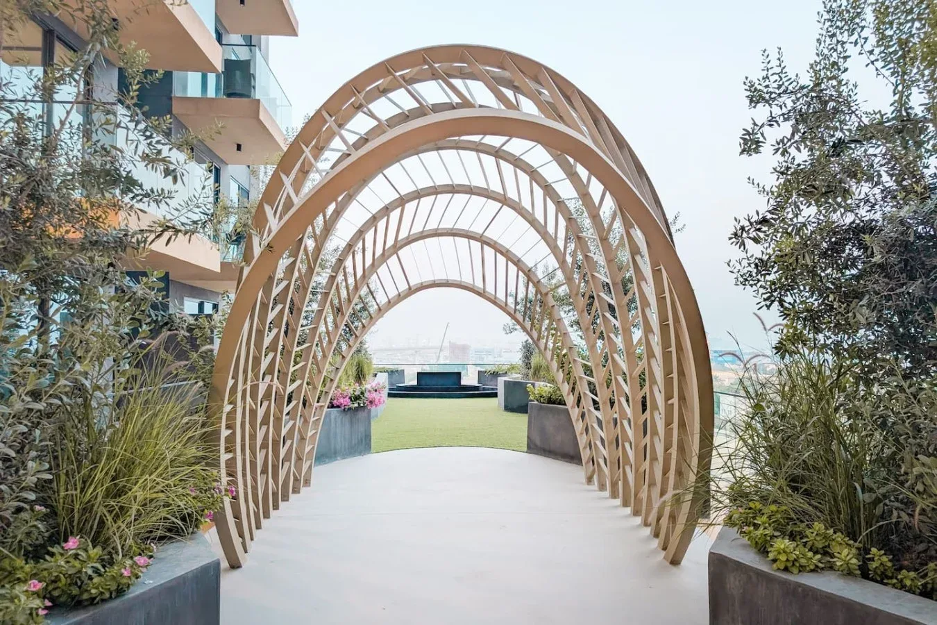 Un sendero ajardinado pasa bajo una serie de arcos curvos de madera.