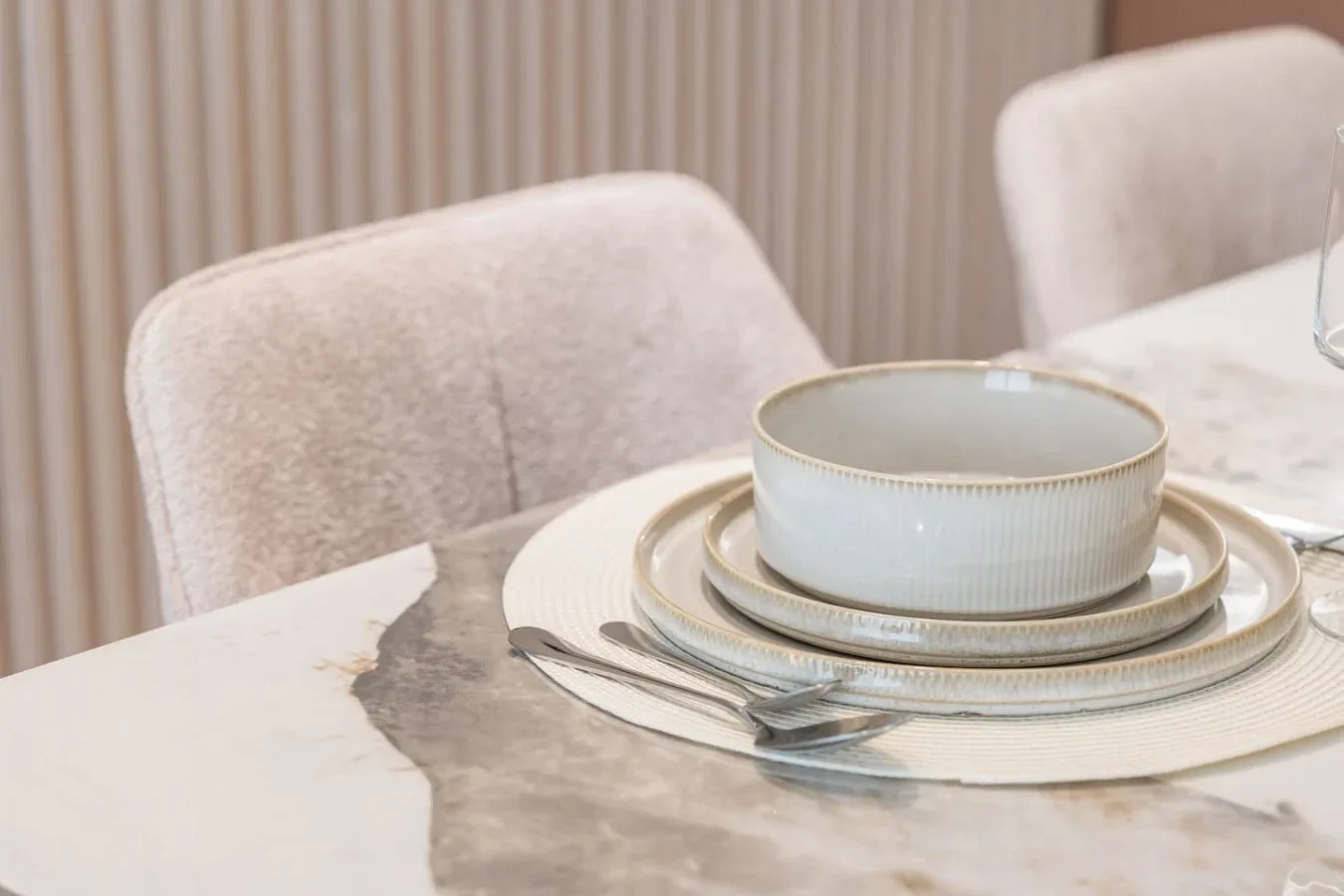 Una mesa de comedor está puesta con platos apilados y un cuenco junto a asientos tapizados.