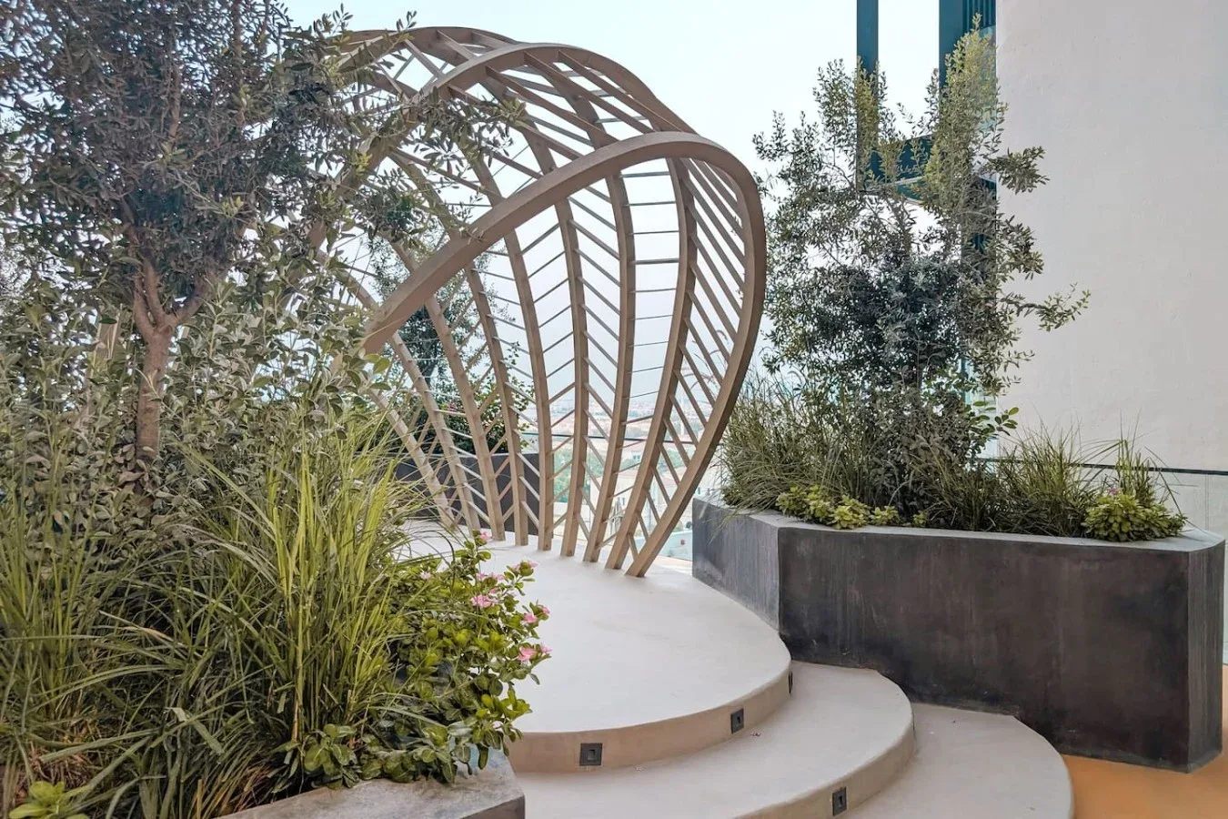 Una zona exterior ajardinada presenta escalones curvos y arcos de madera.