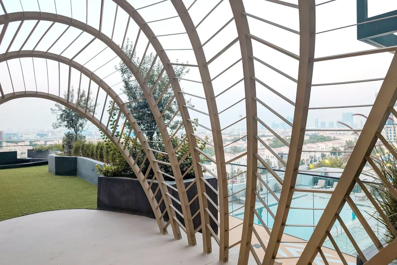 Una terraza exterior curva con cubierta de listones, vegetación y vistas a la ciudad.