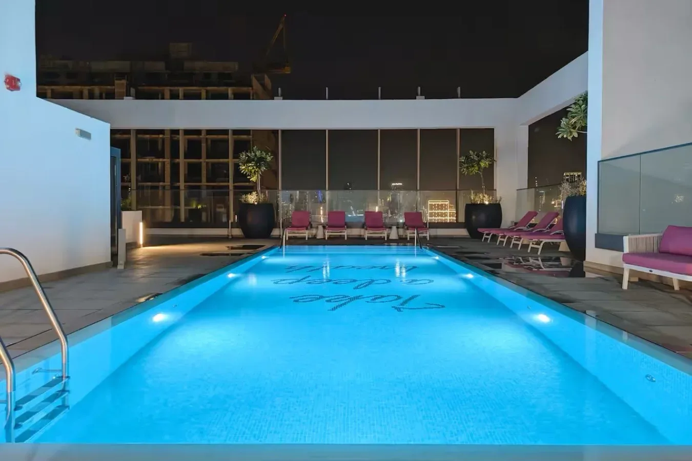 Una piscina iluminada está rodeada de asientos de descanso por la noche.
