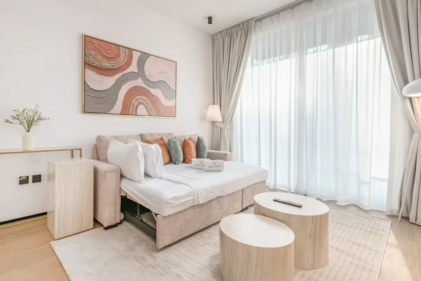 Un dormitorio luminoso con una cama bien tendida junto a una gran ventana con cortinas.
