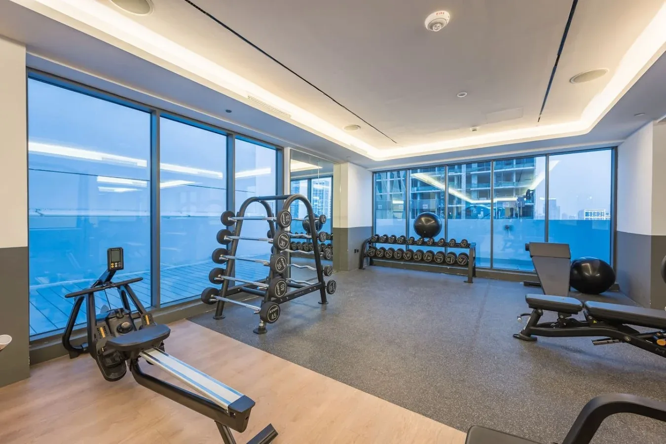 Una sala de ejercicios con pesas y equipos de entrenamiento junto a grandes ventanales.