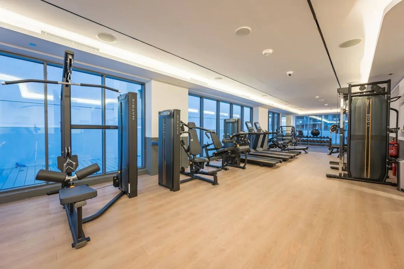 Un gimnasio con máquinas de ejercicio junto a grandes ventanales.