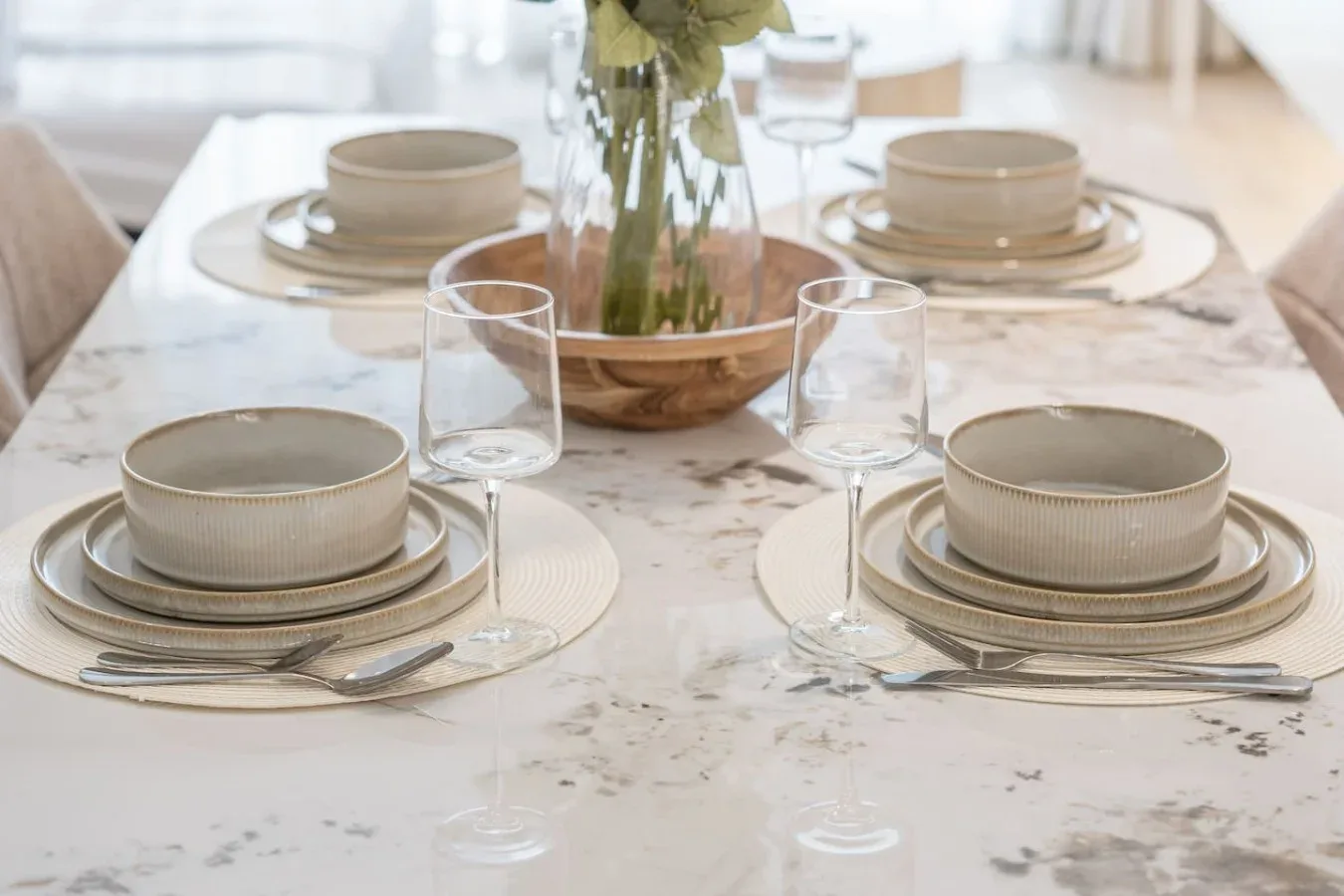 Una mesa de comedor está puesta con platos, vasos y un arreglo floral.