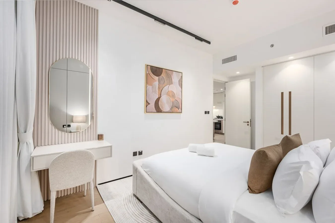 Un dormitorio luminoso con una cama bien tendida y un tocador junto a la ventana.