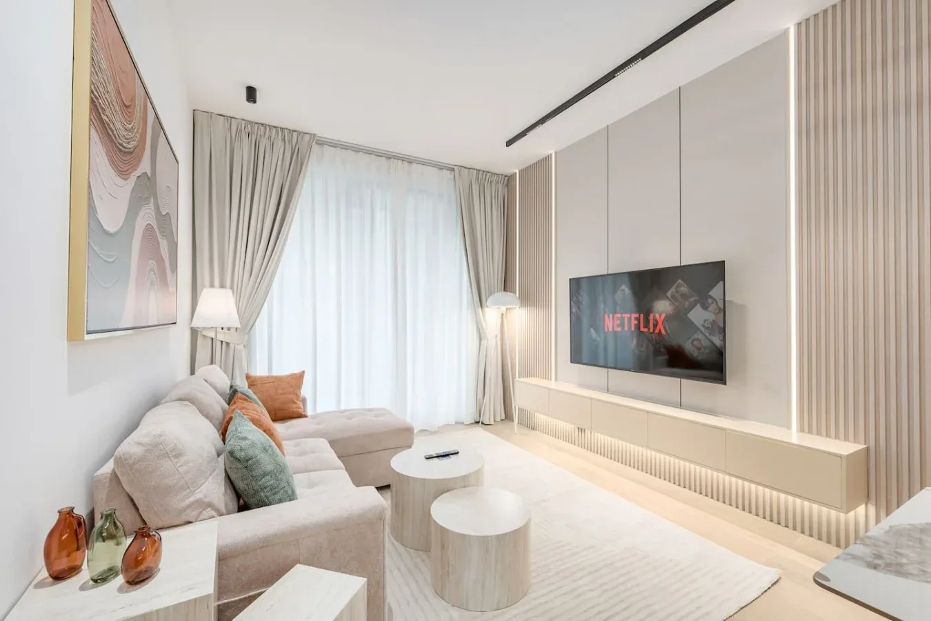 Una sala luminosa con asientos, un televisor y una gran ventana con cortinas.