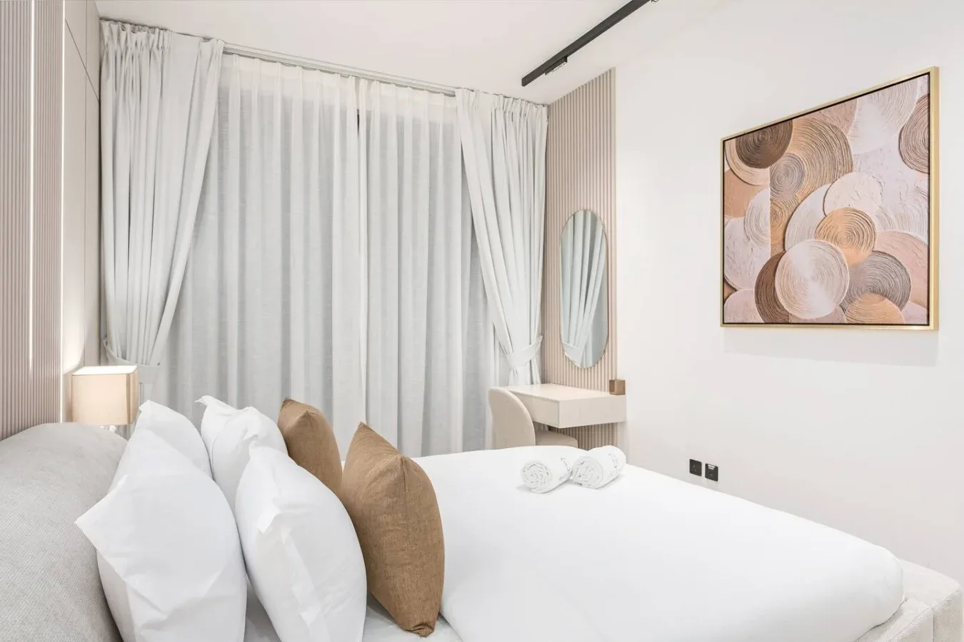 Un dormitorio luminoso con una cama bien tendida y cortinas translúcidas.