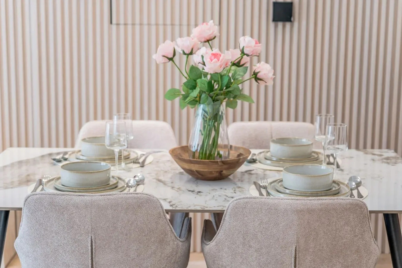 Una mesa de comedor está puesta con platos y un jarrón de flores rosas.