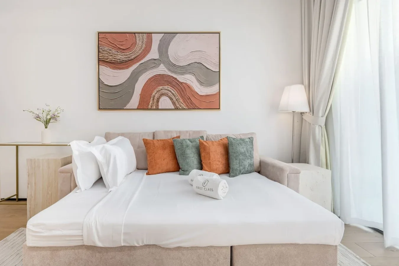 Dormitorio con una cama bien tendida y una obra abstracta encima.