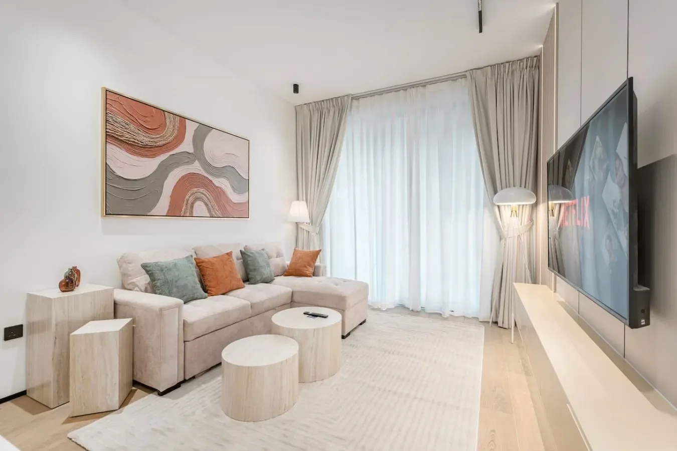 Una sala luminosa con asientos, una gran ventana con cortinas y un televisor en la pared.