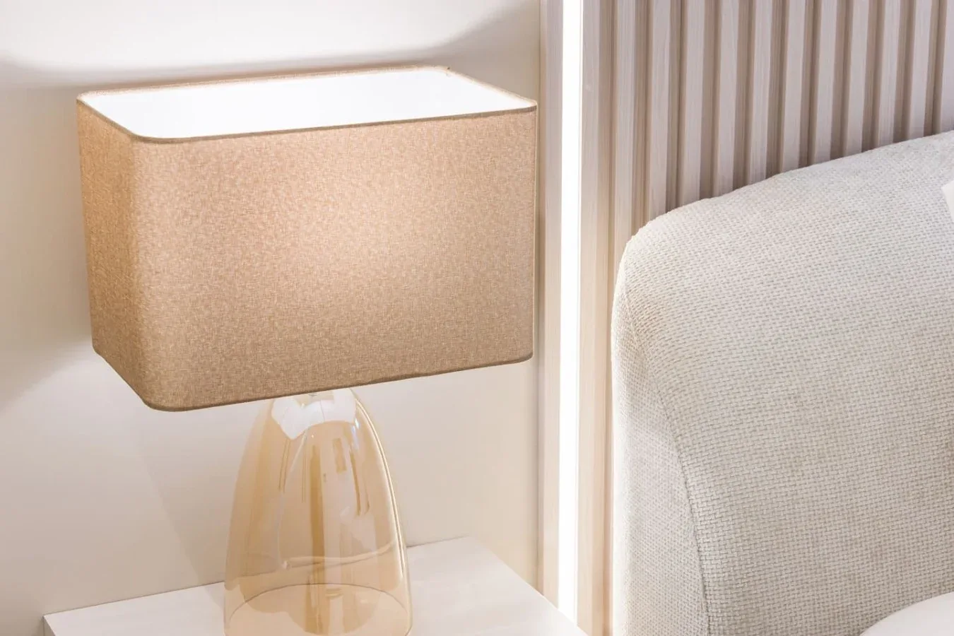 Una lámpara de mesa está junto a un asiento tapizado y una pared de listones verticales.