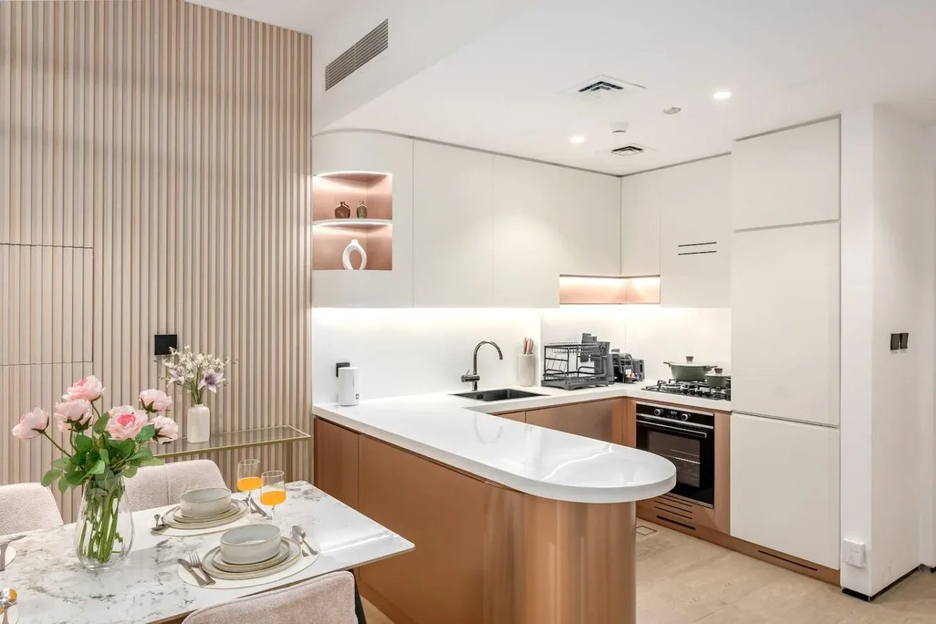 Una cocina moderna y luminosa con encimeras blancas y una mesa pequeña.