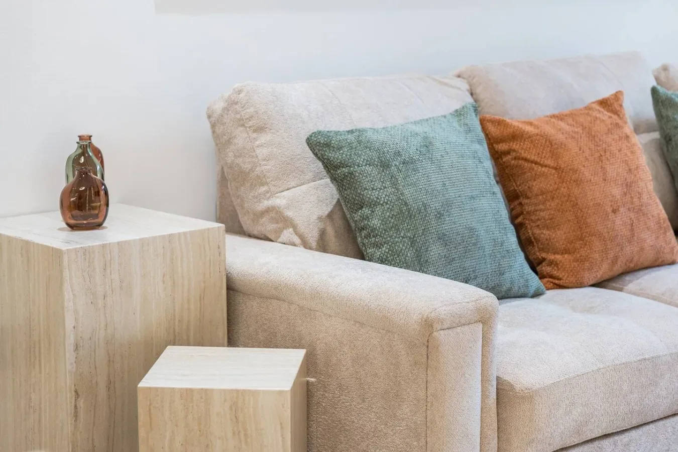 Un sofá de color claro con cojines azules y naranjas está junto a una mesa pequeña.