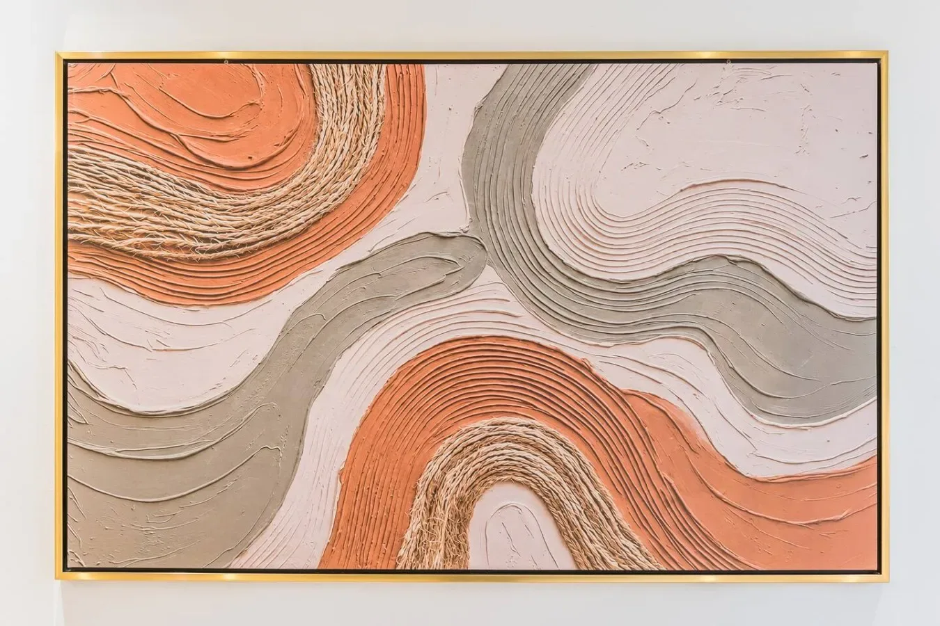 Una obra abstracta enmarcada con formas fluidas naranjas, grises y crema cuelga de una pared.