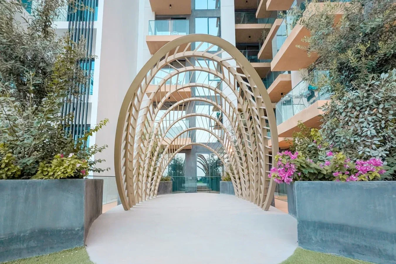 Un sendero ajardinado pasa bajo una serie de arcos curvos entre edificios modernos.