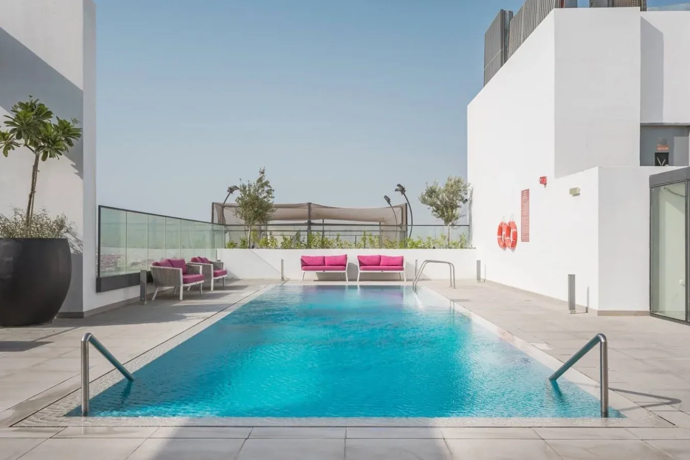 Una piscina al aire libre junto a un edificio blanco y asientos en el patio.