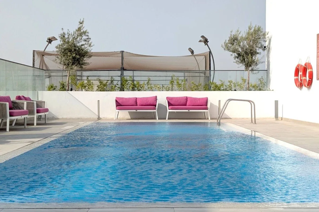 Una piscina al aire libre está rodeada de asientos y una barandilla de vidrio.
