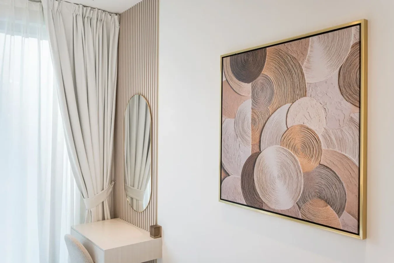 Una esquina luminosa con cortinas recogidas, un espejo y una obra abstracta enmarcada.