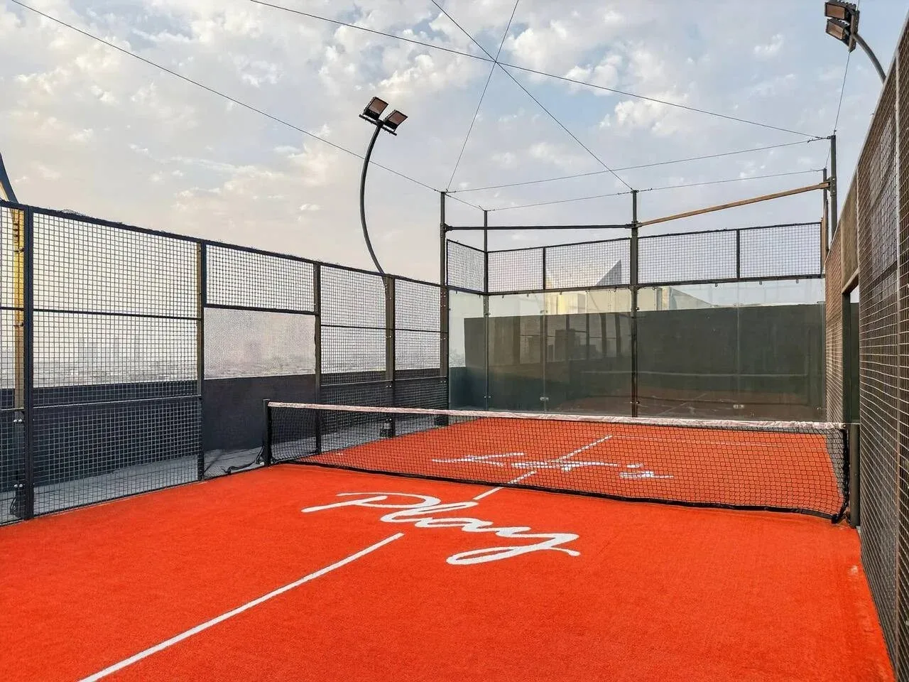 Una cancha deportiva al aire libre con piso naranja brillante y cercas de malla.