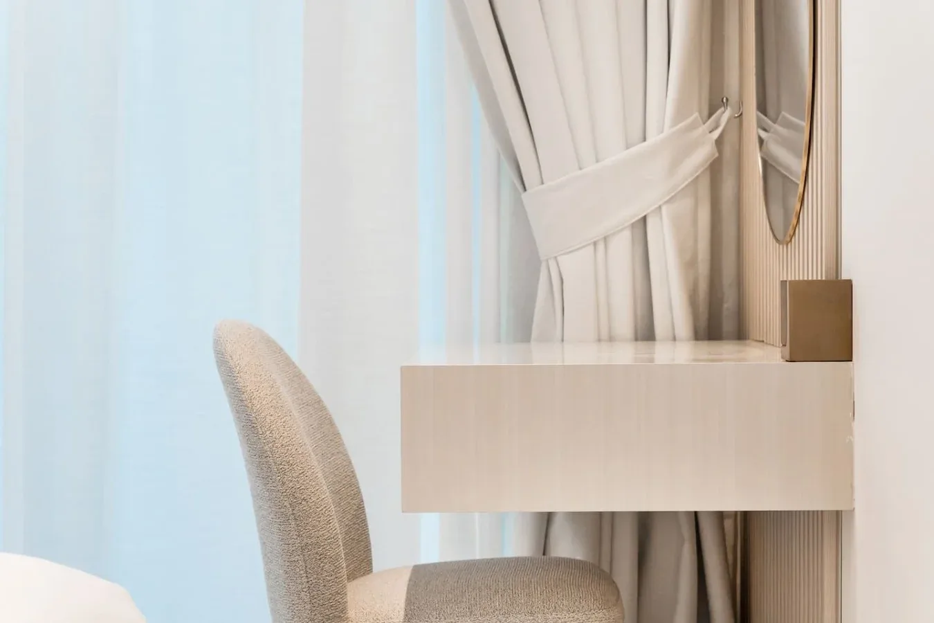 Una esquina de dormitorio con una silla acolchada junto a una cómoda y cortinas.