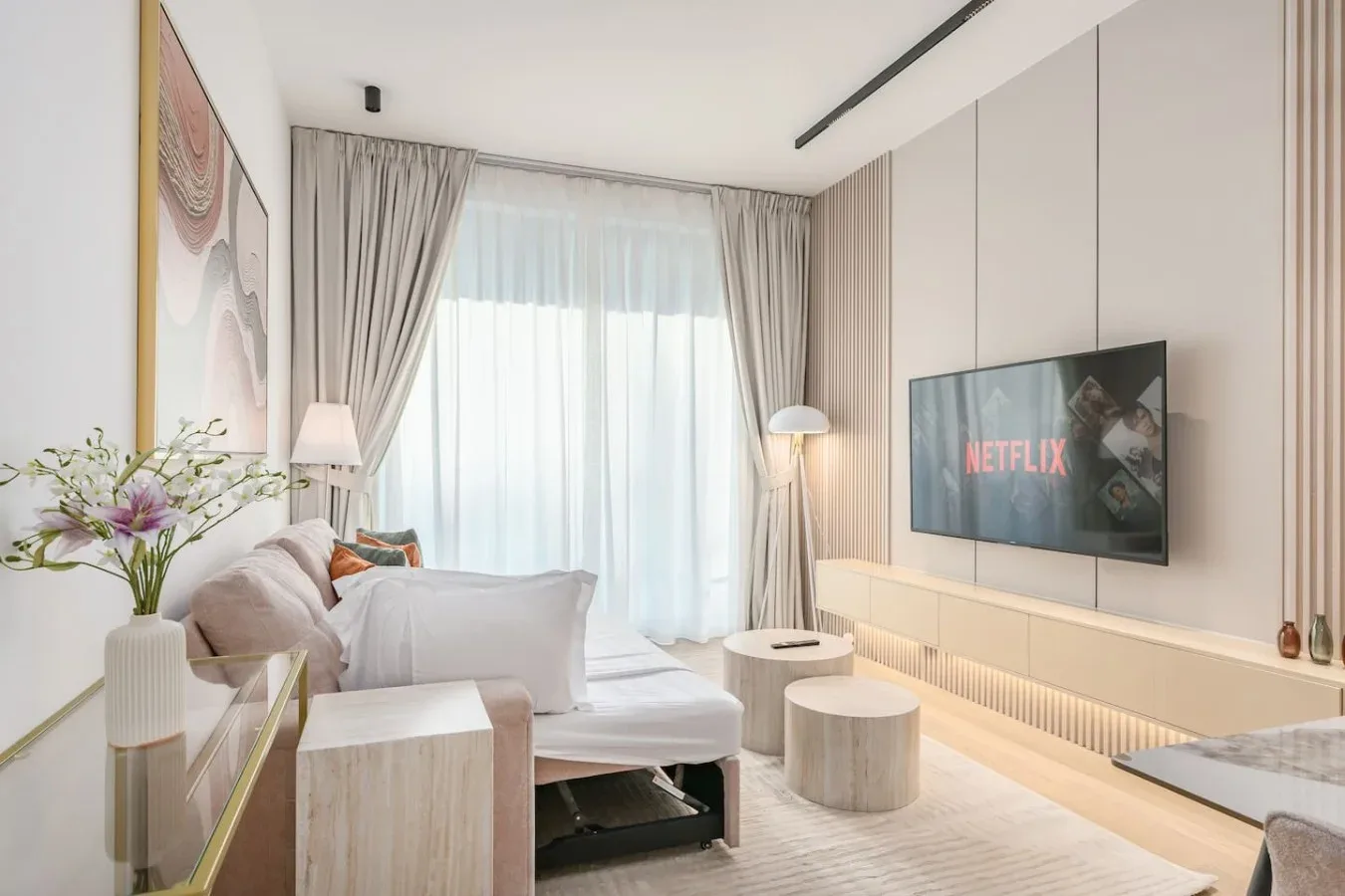 Una sala luminosa con sofá, televisor y grandes ventanas con cortinas.