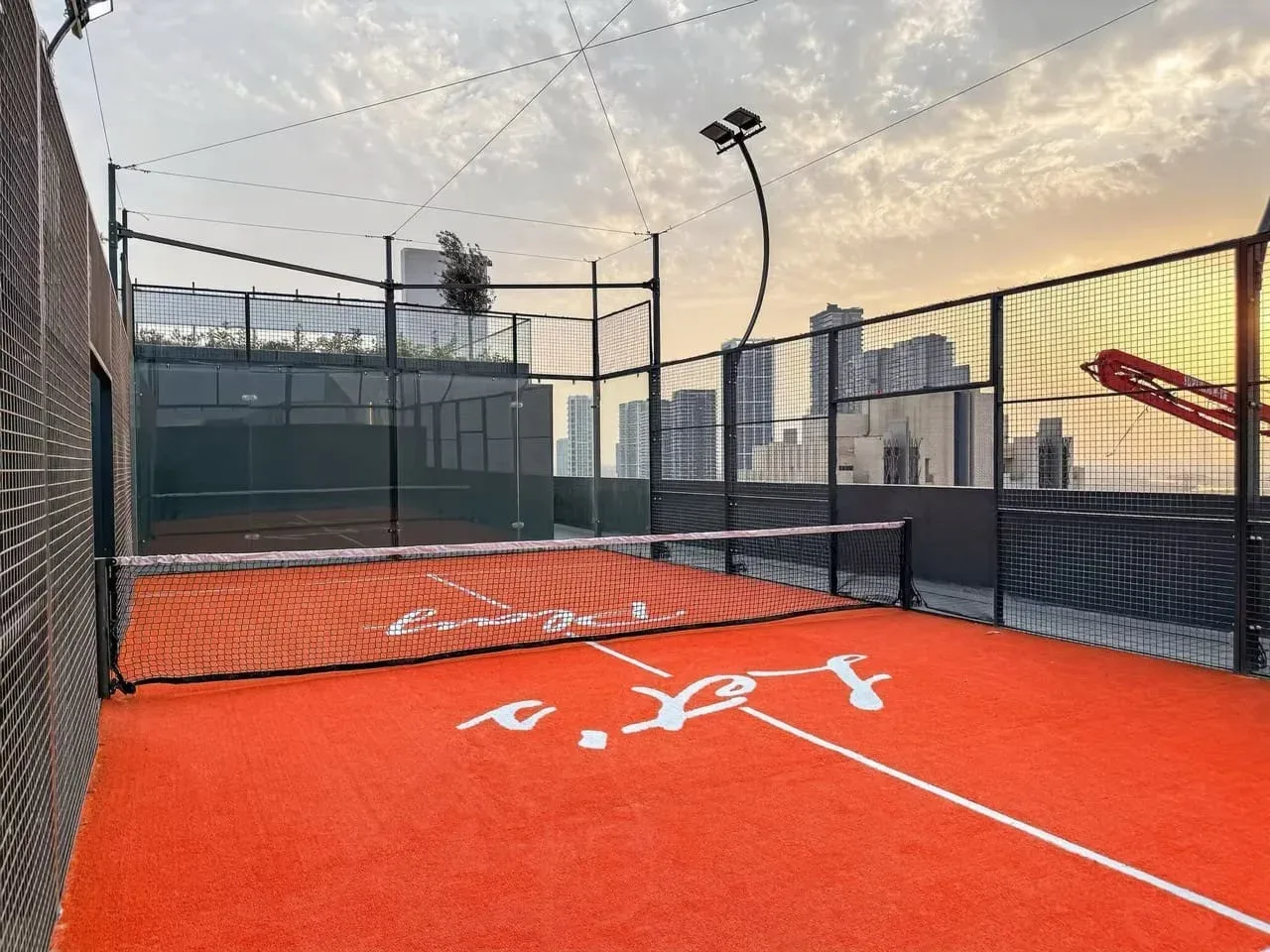 Una pista de pádel al aire libre, con una red y edificios de la ciudad más allá de la valla.