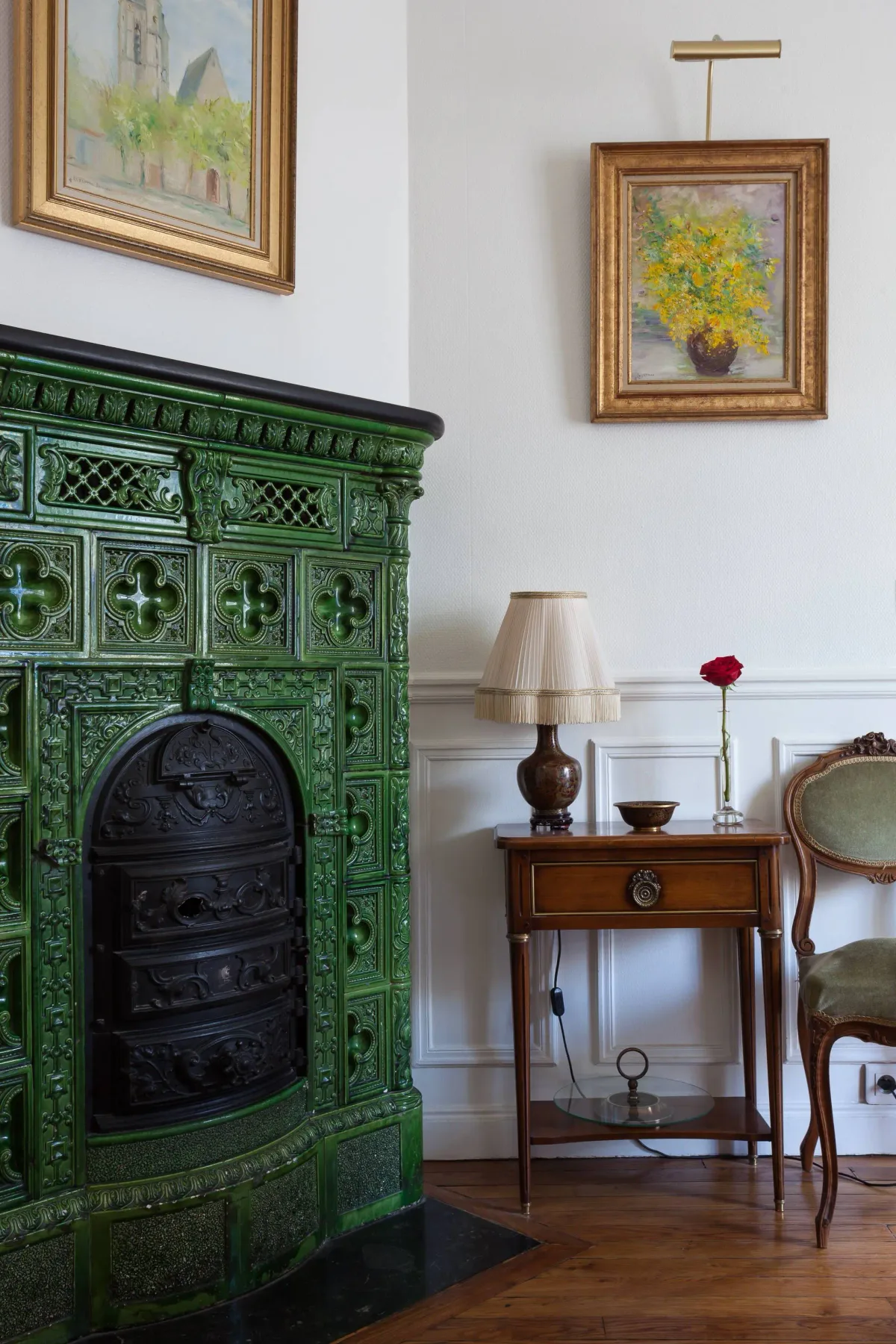 A traditional room with a green tiled fireplace, framed paintings, and a wooden side table.