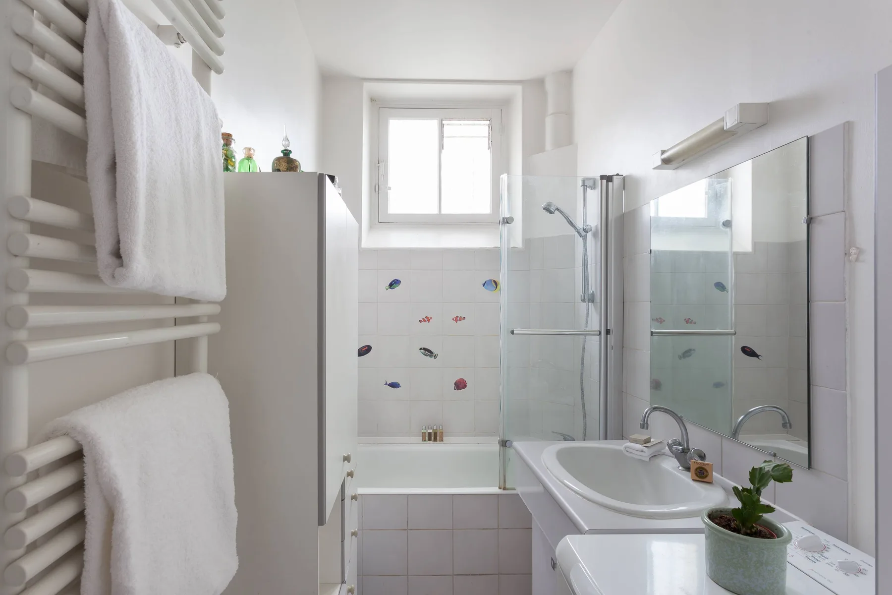 A bright bathroom with a bathtub, glass shower screen, and sink.
