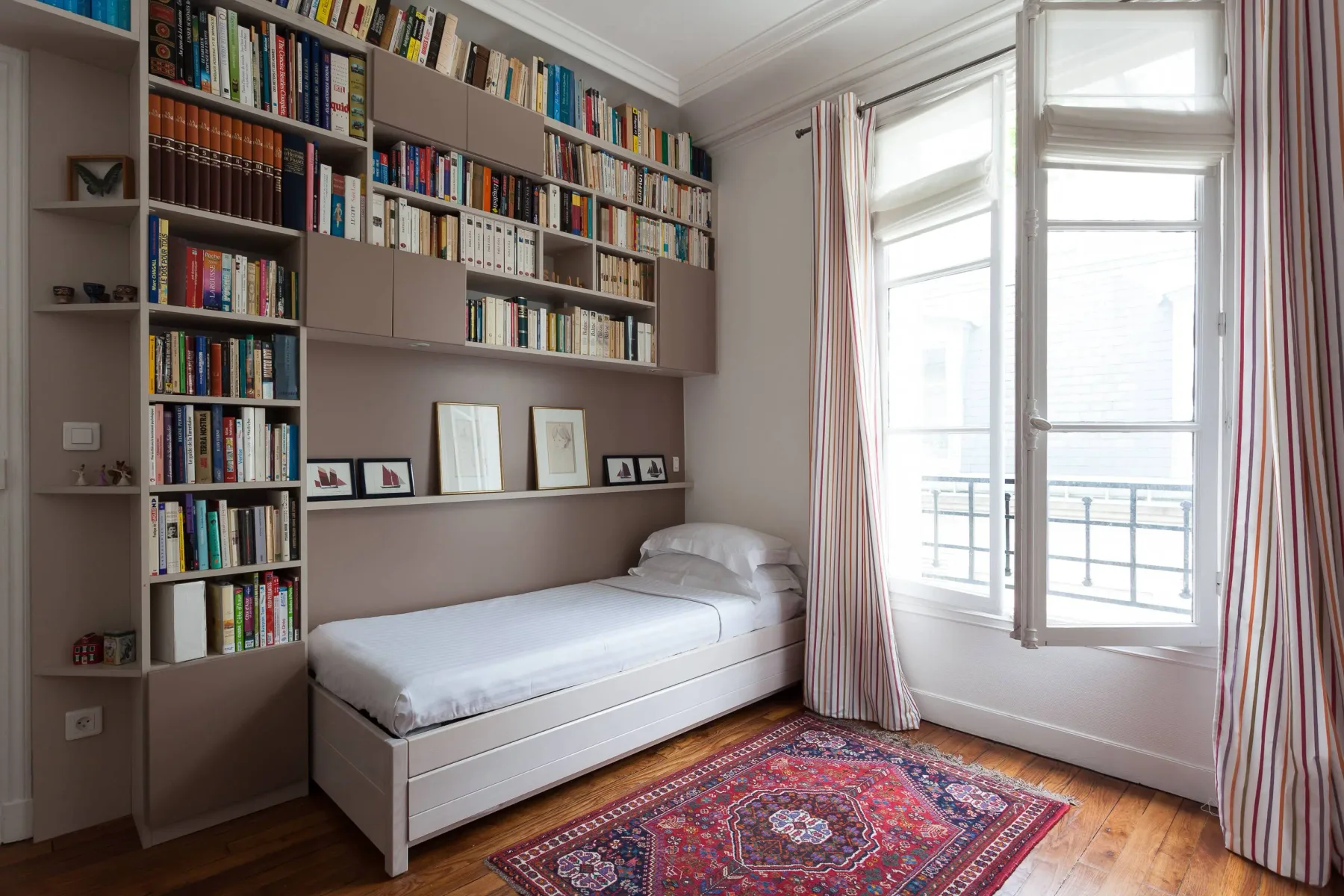 A bright bedroom with a single bed beneath wall-length bookshelves.