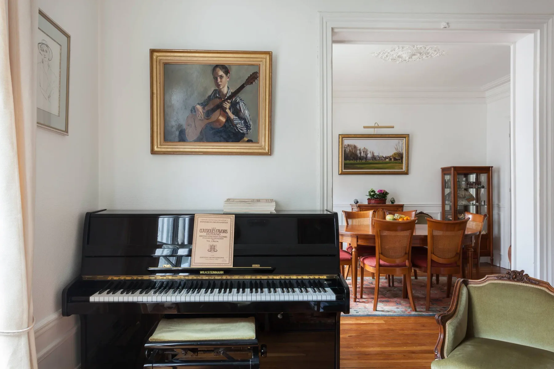 A piano sits beneath framed artwork beside a dining area.