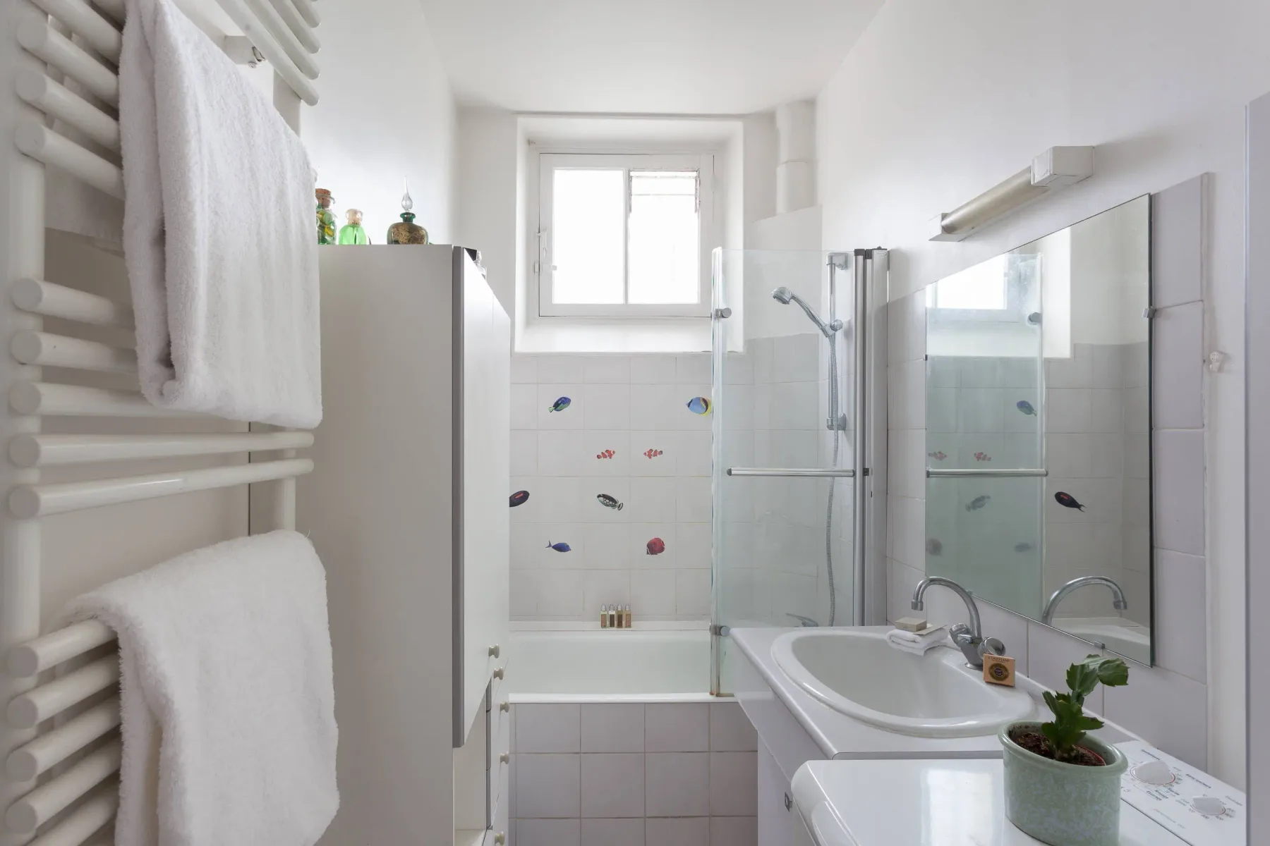 A bright bathroom with a bathtub, glass shower screen, and sink.