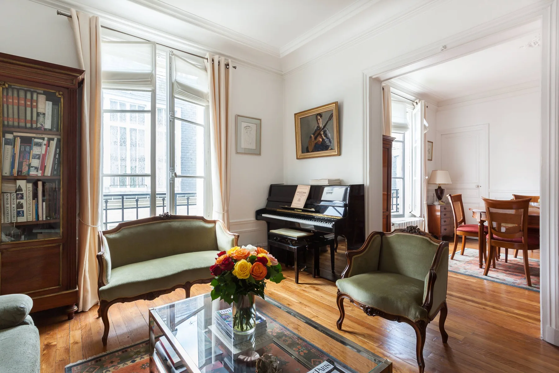 A bright living room with green seating, a piano, and tall windows.