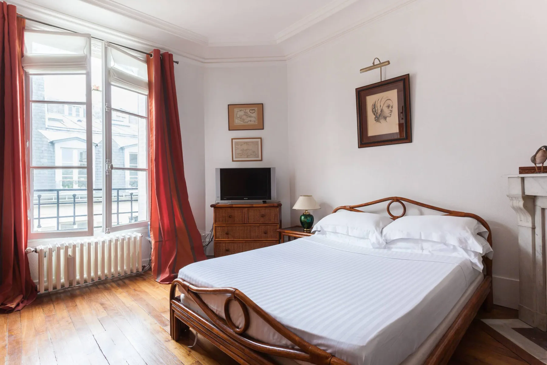 A bedroom with a bed, wooden dresser, and tall windows.