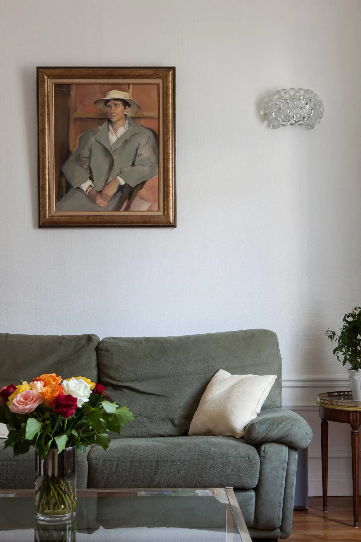 A living room with gray seating, a framed portrait, and flowers on a glass table.