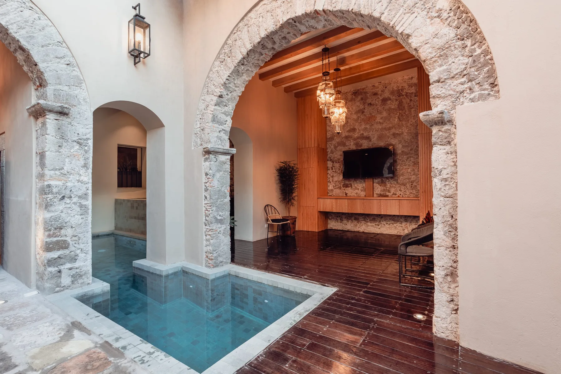 A small indoor pool sits beside a lounge with a television and exposed wooden ceiling beams.