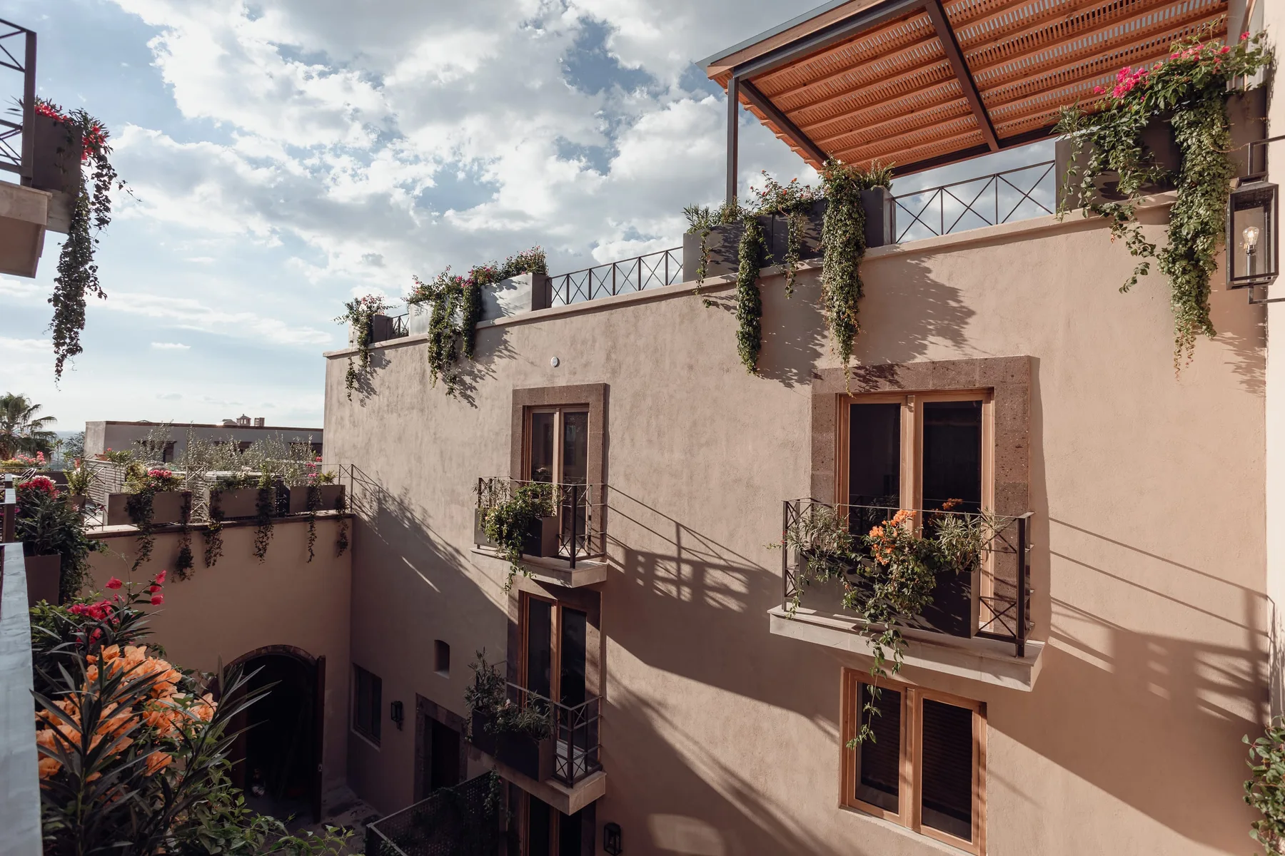 A sunlit courtyard framed by balconies, potted plants, and a covered terrace.