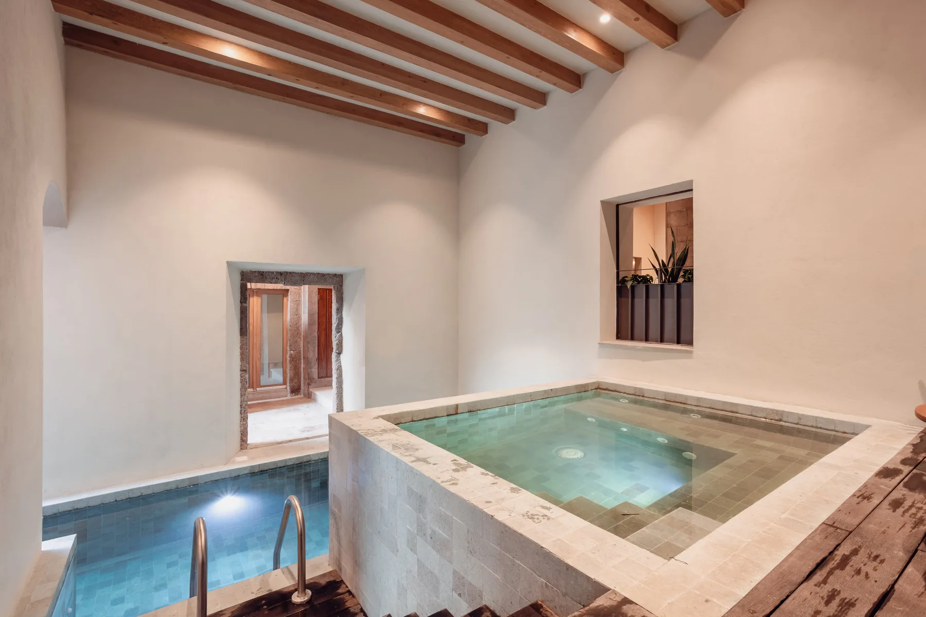 An indoor pool area with a raised square pool and exposed wooden ceiling beams.