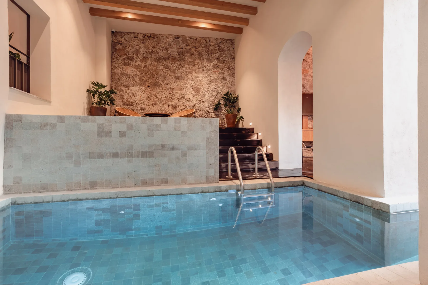 An indoor swimming pool with tiled walls and a stone feature wall.