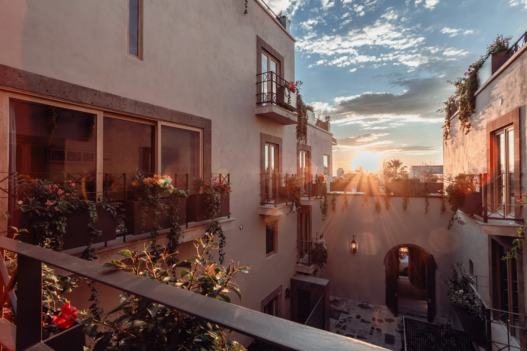 A sunlit courtyard between buildings, with balconies and plants.