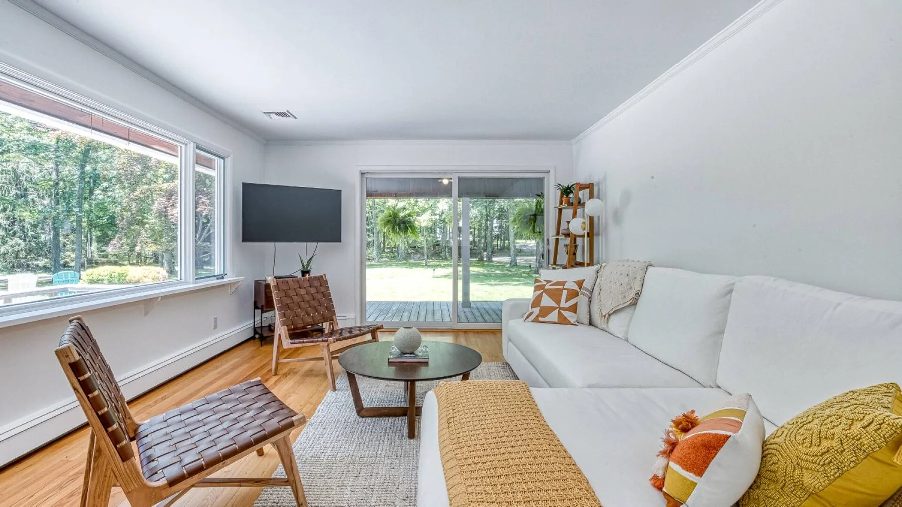 A bright living room with seating, a coffee table, and large windows overlooking greenery.