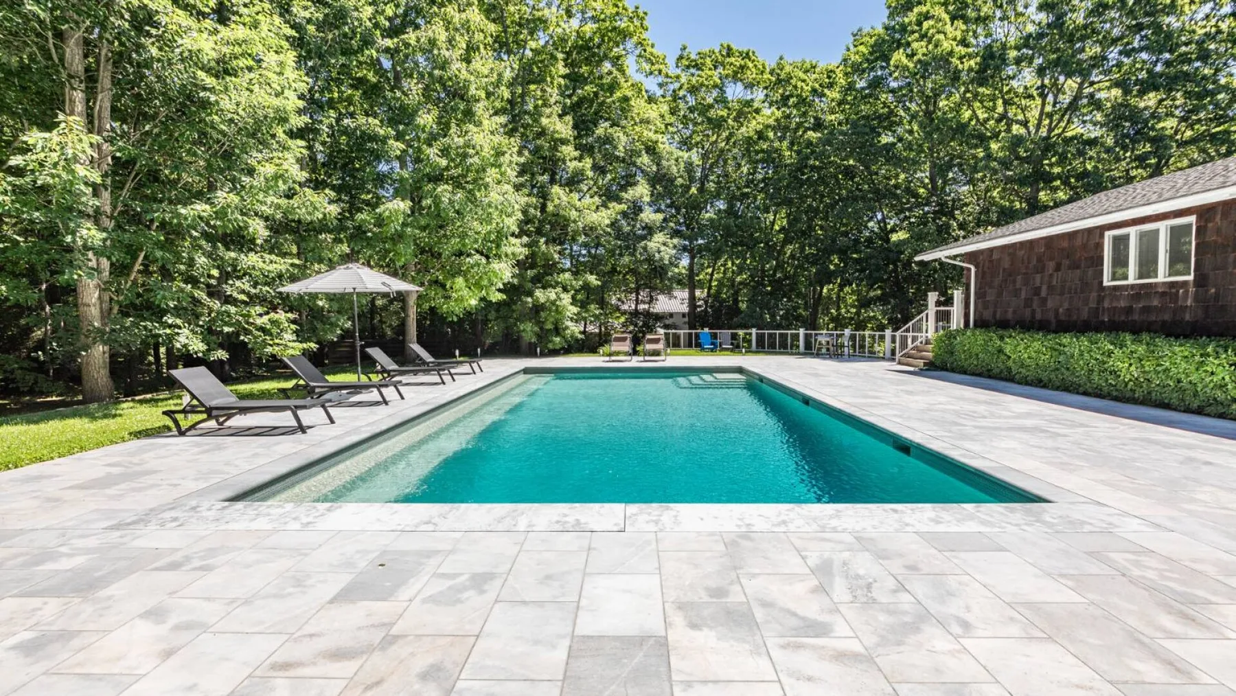 A swimming pool with a paved deck, loungers, and surrounding trees.