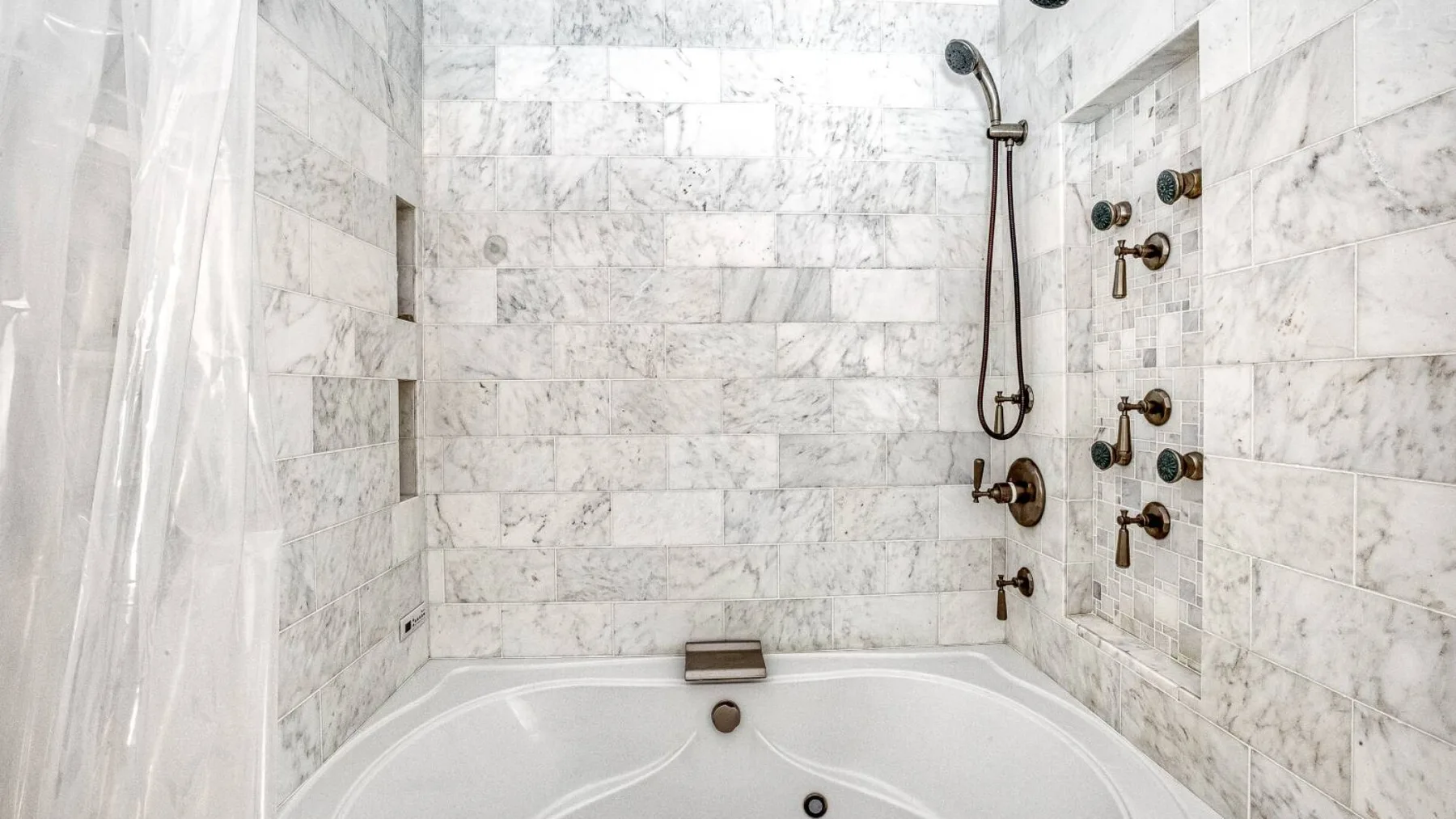 A marble-tiled bathroom with a bathtub and wall-mounted shower fixtures.